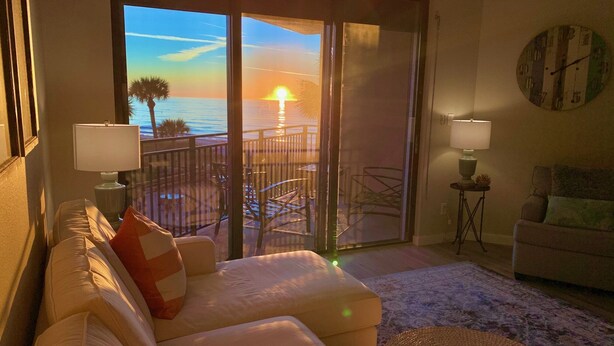 A living room with a sofa, a coffee table, and a view of the sunset through a sliding glass door. - Breathtaking sunsets and sunrises! (Indian Rocks Beach)