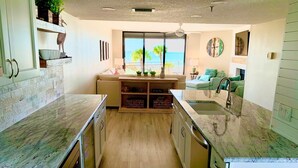 A modern kitchen with a central island, wooden cabinets, and a view of the ocean through large windows. - Breathtaking sunsets and sunrises! (Indian Rocks Beach)