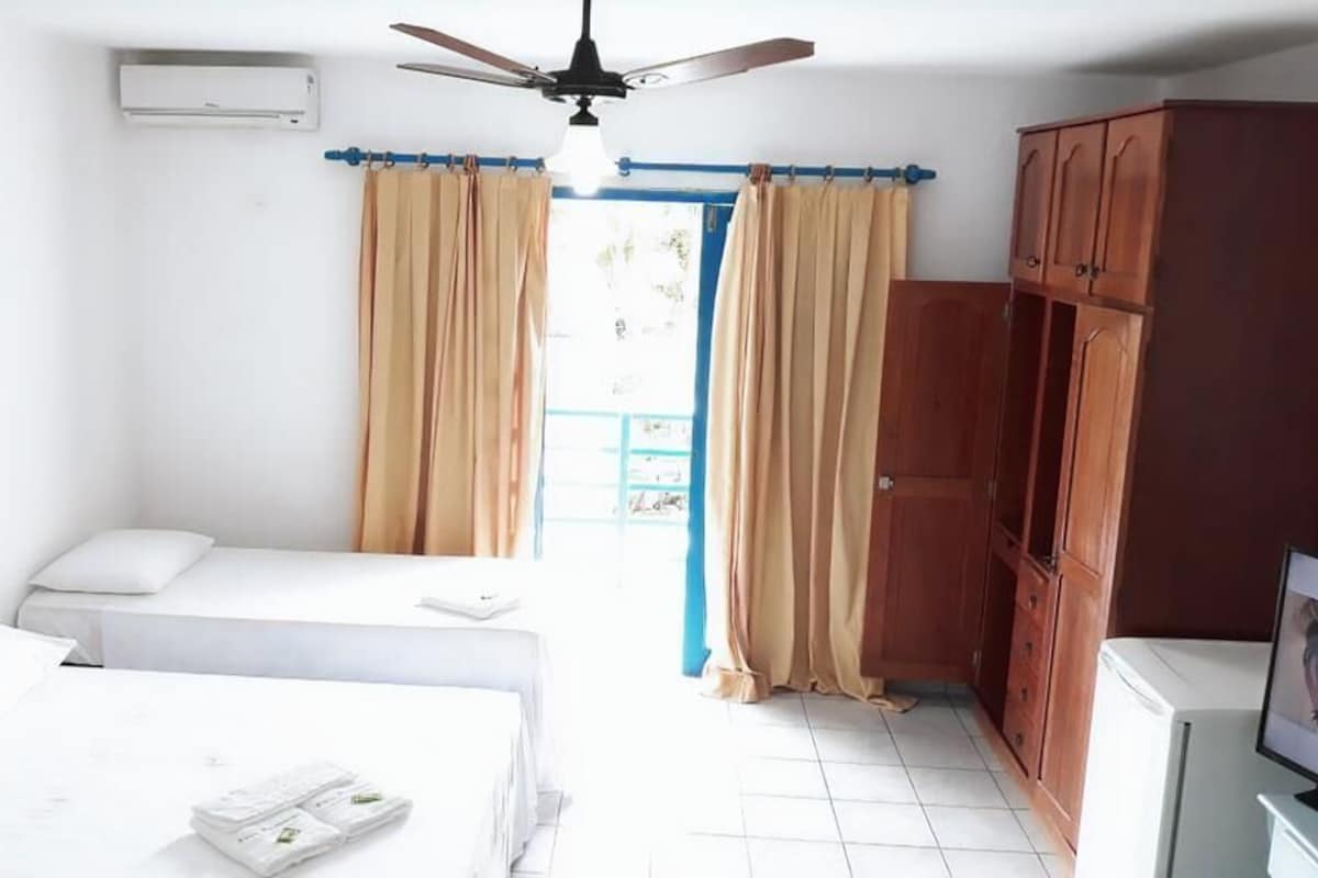 A room with two beds, a ceiling fan, an air conditioning unit, wooden cabinets, and a television.