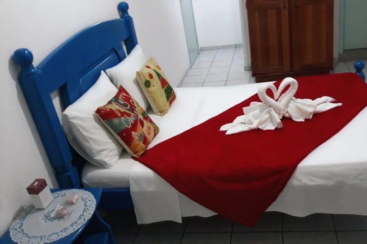 A bed with a red blanket and white sheets, a blue headboard, and two pillows with festive designs.