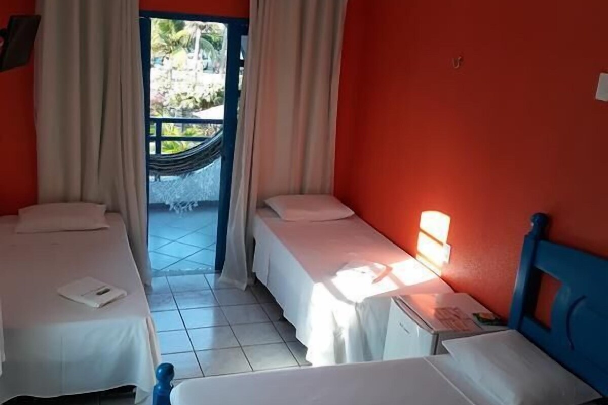 A hotel room with two single beds, a small table with a lamp, and a view of a garden through a window.