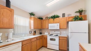 A kitchen with wooden cabinets, a white stove, a microwave, and a refrigerator. - Sunshine Villa by VillaDirect (Kissimmee)