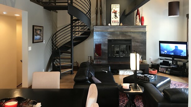 A modern living room with a spiral staircase, a fireplace, a television, and a ski-themed sign.