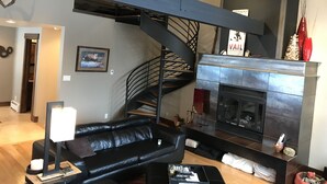 A modern living room with a black leather sofa, a fireplace, and a spiral staircase.