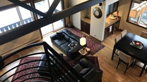 A modern living space with a black leather sofa, a dining table with chairs, a staircase, and a kitchen area.