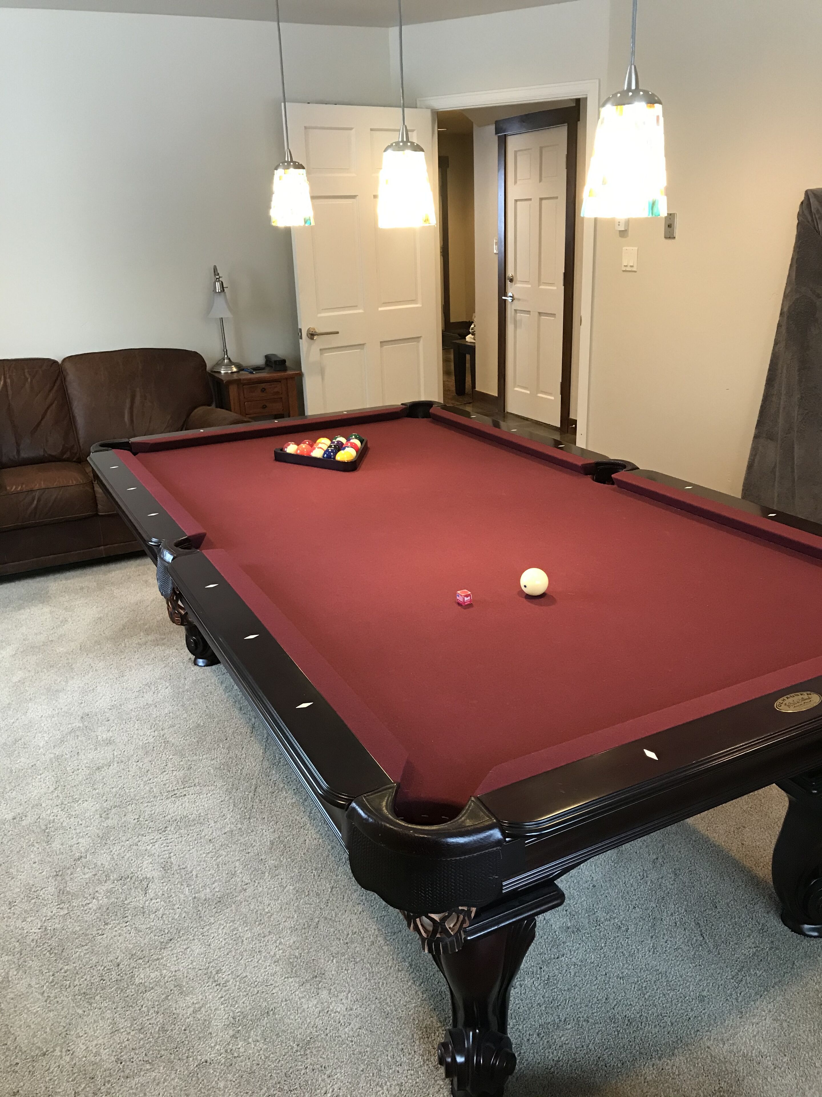 Une table de billard avec des billes, un canapé en cuir marron et des lampes suspendues.