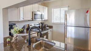 Una cocina moderna con armarios blancos, electrodomésticos de acero inoxidable, encimeras de granito y horno empotrado.