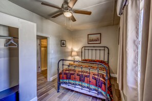 Une chambre à coucher avec un lit, un ventilateur de plafond, une lampe de chevet, une porte et une fenêtre avec des rideaux.