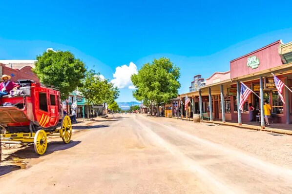 A historic street with a red carriage, storefronts, and American flags.