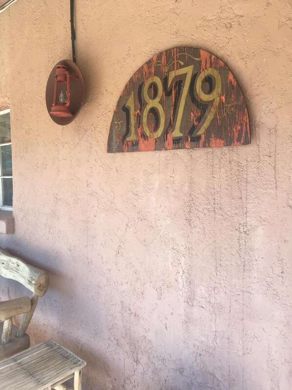 Una pared rústica con un letrero desgastado que dice "1879" y un farol.