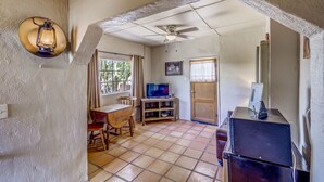 A room with a ceiling fan, a television on a wooden stand, a refrigerator, and a dining table with chairs. - Stay at the Historic San Jose House Room 4 Doc Holliday (Tombstone)