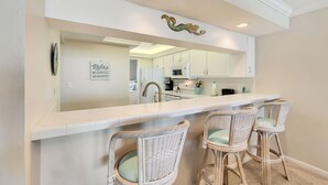 A kitchen with a white countertop, two wicker bar stools, and a decorative wall piece above the counter.
