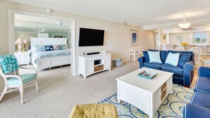 A living room with a bed, a TV, a white entertainment unit, a blue sofa, and a patterned rug.