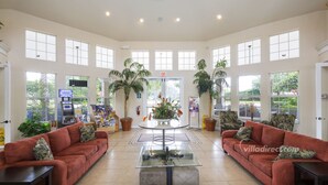 A spacious lobby with a central round table, two sofas, and a small coffee table. There are potted plants and a fire extinguisher on the wall. - Sable Palms Villa by VillaDirect (Kissimmee)