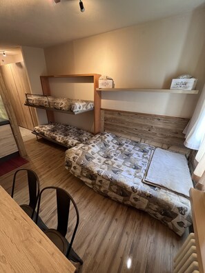 Habitación con literas, un cabecero de madera, una mesita con sillas y una estantería con una caja que dice 'HOME'.