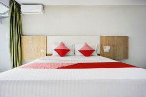 A hotel room with a large bed, two red pillows, a white and red bedspread, a wooden headboard, and an air conditioning unit. - Collection O Gapura Hotel Near Parapat Penatapan Danau Toba (Parapat)