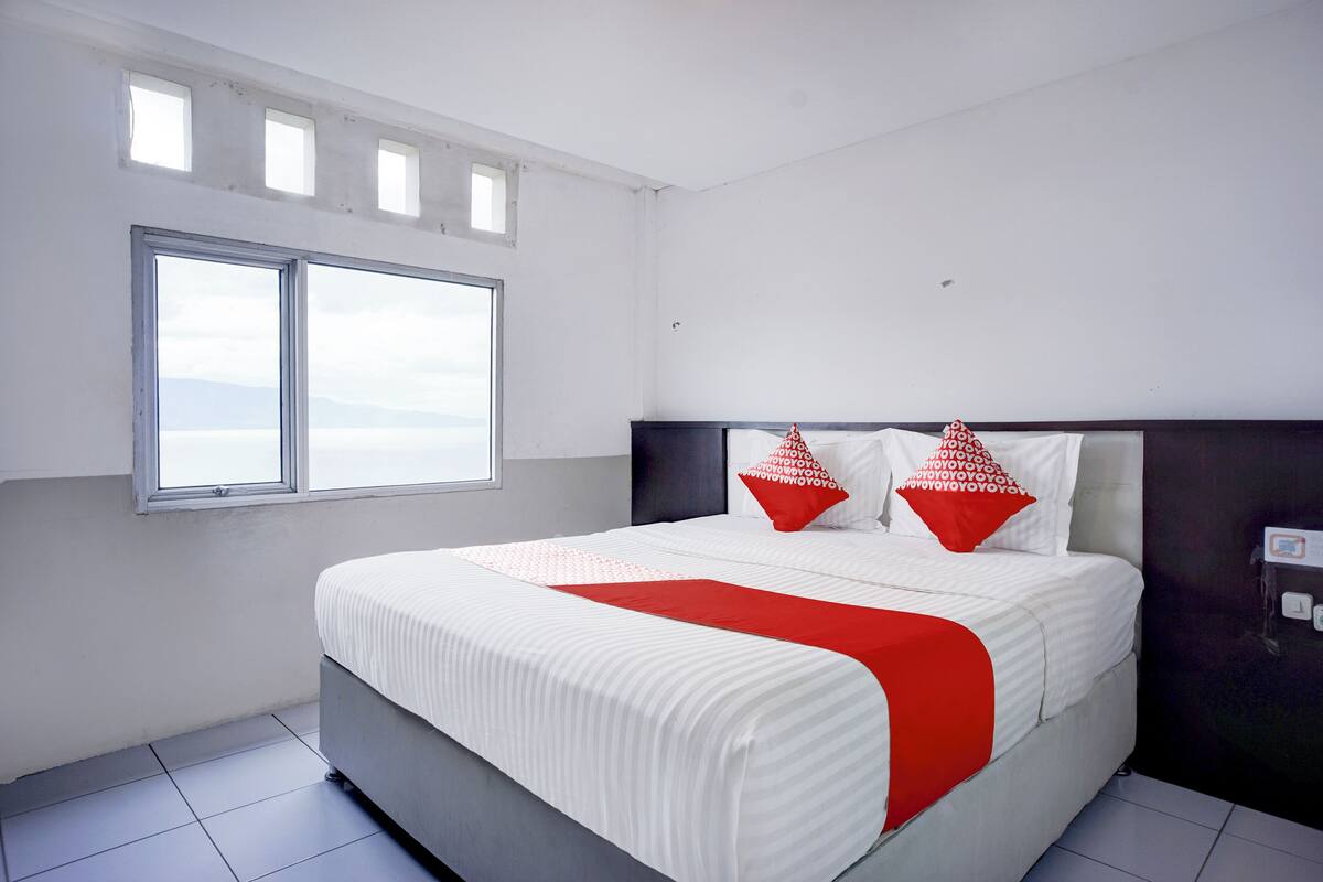 A modern bedroom with a large bed, two windows, and a view of the sky.