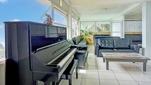 Un vaste salon agrémenté d’un magnifique piano à queue, de sièges confortables et de grandes fenêtres offrant une vue sur l’extérieur.