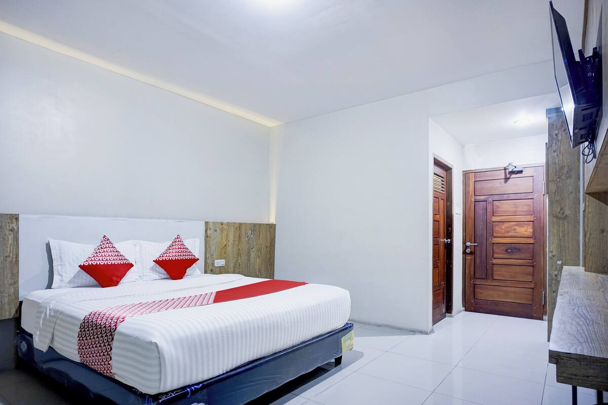 A neatly made bed with a white and red bedspread, two red pillows, and a wooden headboard.