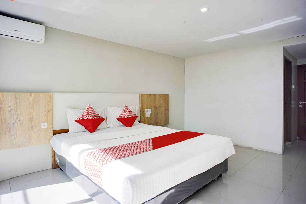 A modern hotel room with a large bed, a wooden headboard, and a red and white bedspread.