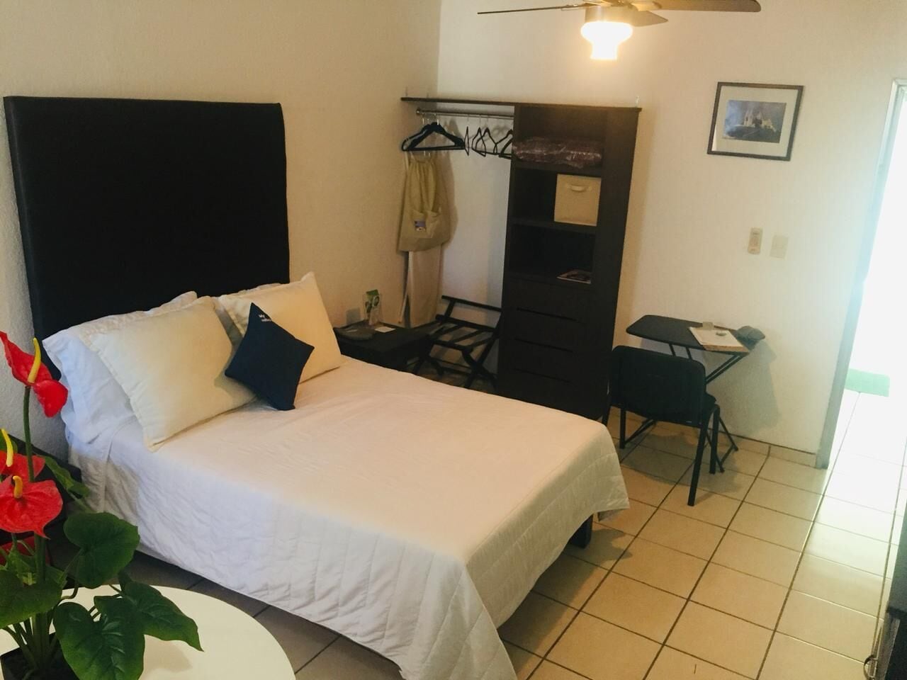 A hotel room with a bed, a desk, a chair, a coat rack, and a small table.