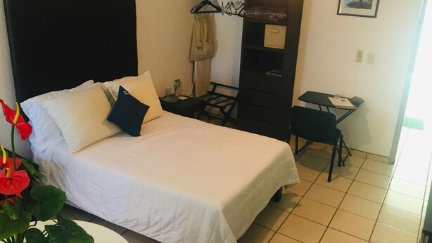 A hotel room with a bed, a desk, a chair, a coat rack, and a small table. - My Suite Ejecutivas (Culiacán)