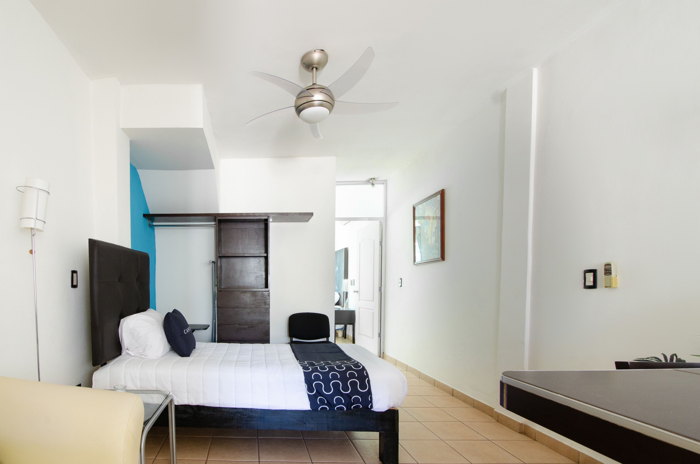 Habitación de hotel con cama, escritorio, silla, ventilador de techo y televisión.