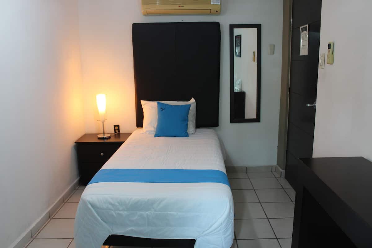 A hotel room with a bed, a nightstand, a bedside lamp, a mirror, and a door.