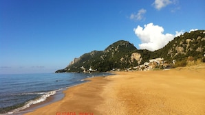 Una playa con huellas, cielo despejado y una montaña al fondo.