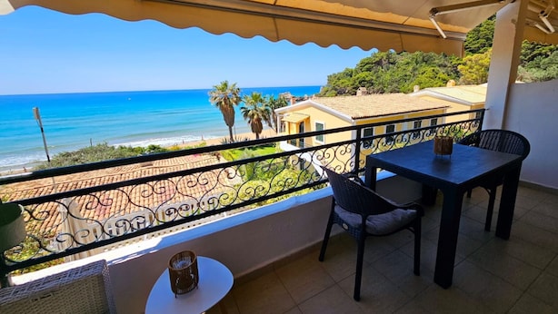 Un balcón con vista al mar, una mesa y sillas.