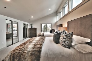 Ein modernes Schlafzimmer mit einem großen Bett, einer Kopfteil und Blick durch eine Glastür.
