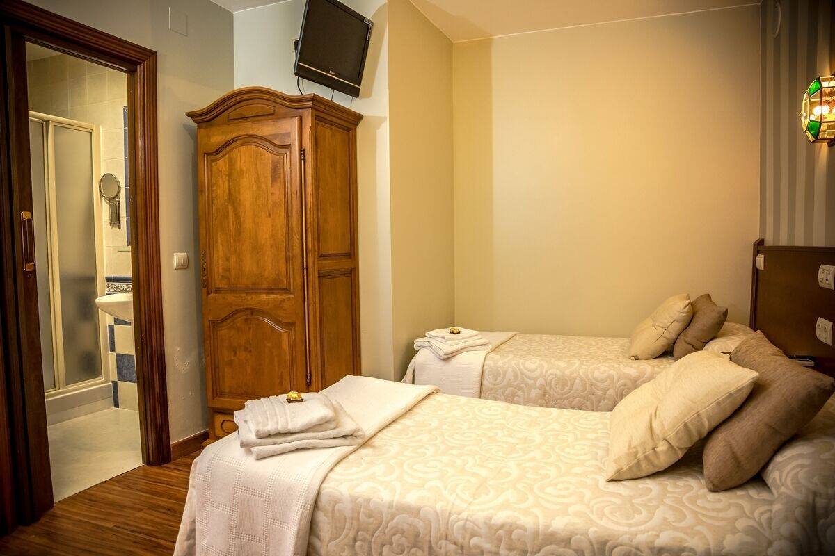 A hotel room with two beds, a wooden wardrobe, a television, and a bathroom visible through an open door.