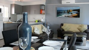 A modern living room with a dining area, grey cabinets, a painting of a beach, and a ceiling fan.