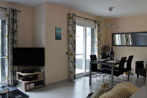 Una sala de estar con un televisor de pantalla plana, una mesa de comedor con sillas, un sofá y un espejo grande.