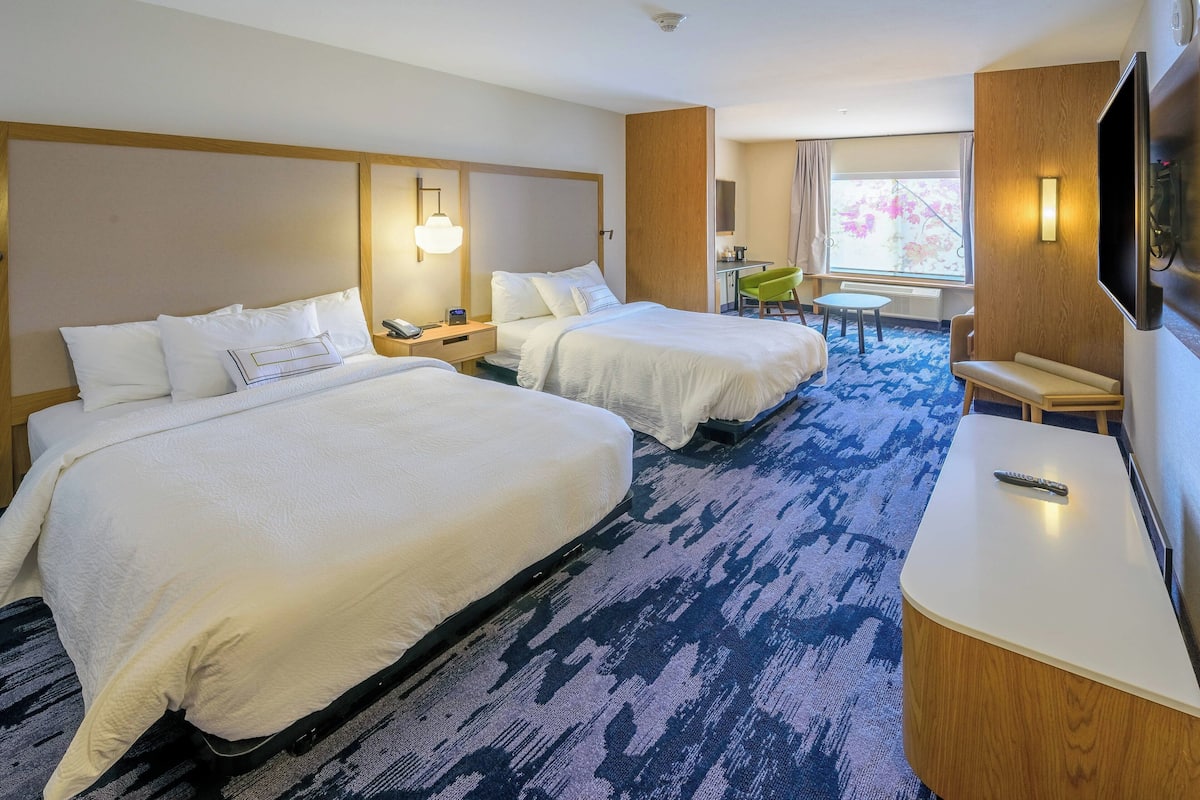 A hotel room with two beds, a desk, a chair, a TV, and a window with a view.