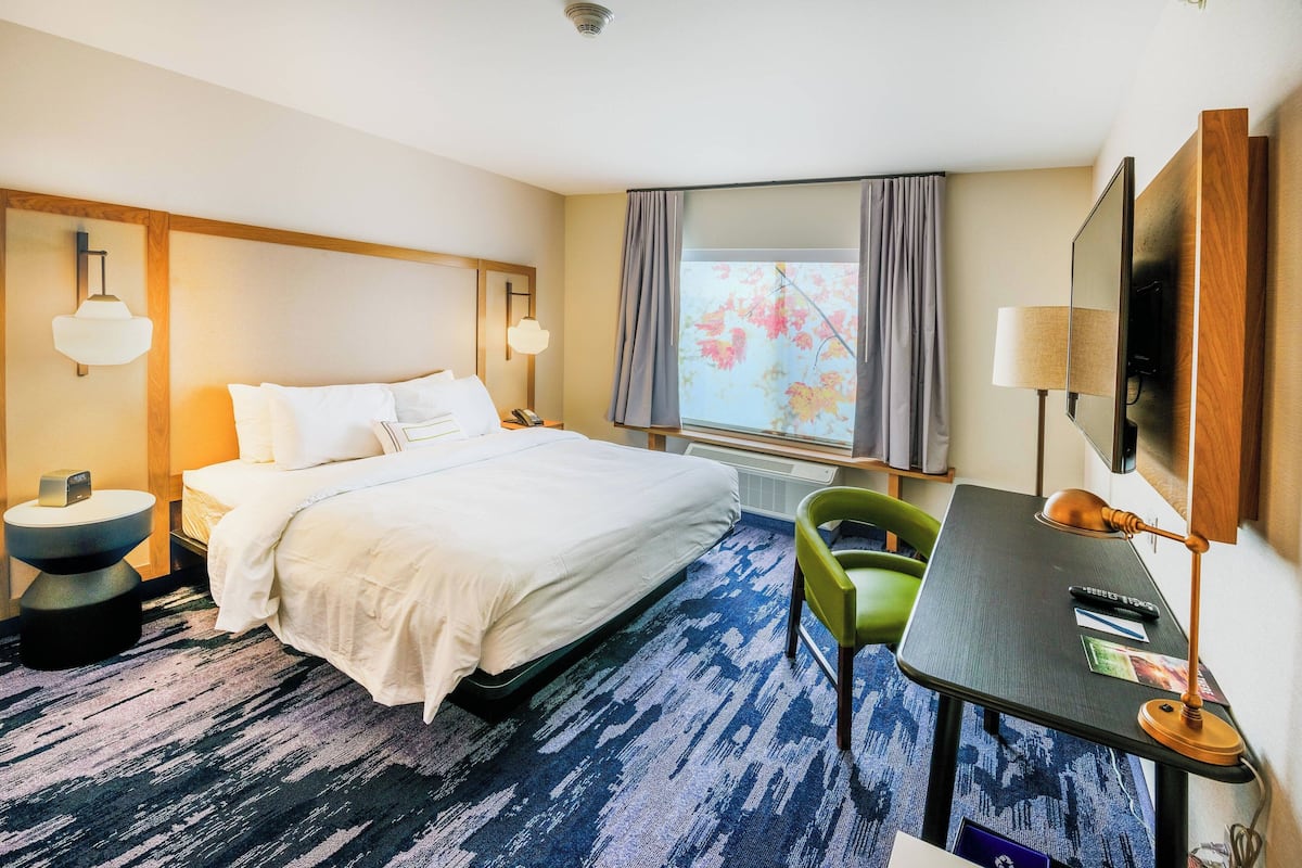 A hotel room with a bed, a desk, a chair, a TV, and a window with curtains.