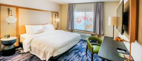 Habitación de hotel con cama, escritorio, silla, televisor y ventana con cortinas.