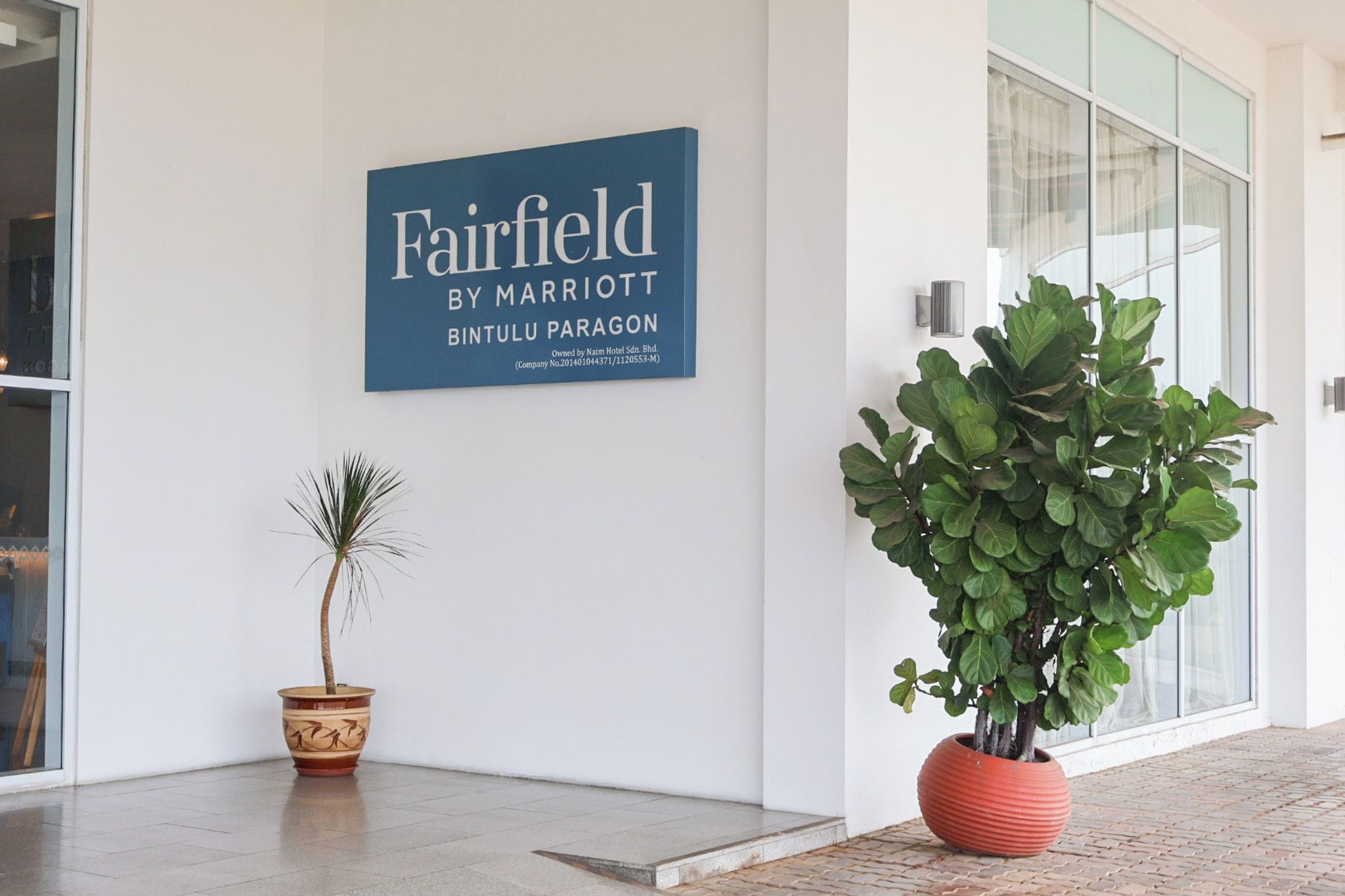 A hotel sign with the name 'Fairfield by Marriott Bintulu Paragon' and a potted plant in front.