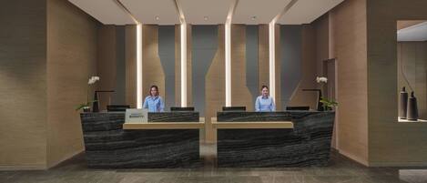 Uma área de recepção com dois recepcionistas, um balcão de mármore e iluminação moderna.