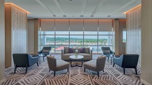 A modern hotel lobby with a large window offering a city view, a central seating area with a sofa and chairs, and patterned carpet. - Fairfield by Marriott Bintulu Paragon (Bintulu)