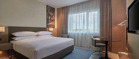 Ein Hotelzimmer mit einem großen Bett, einem Schreibtisch, einem Stuhl, einem Fernseher und einem Fenster mit Vorhängen.