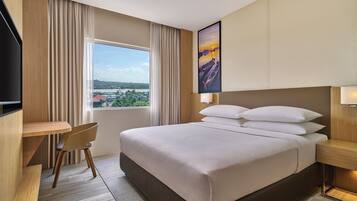A hotel room with a large bed, a desk, a chair, and a window with a view of a cityscape.