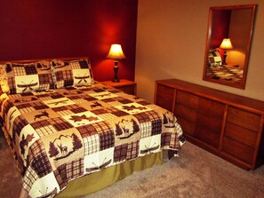 A bed with a quilt featuring animal prints, two bedside lamps, a mirror, and a wooden dresser.
