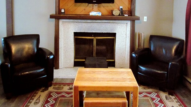A living room with two black leather chairs, a wooden table, a fireplace, and a mounted television. - Paintbrush North- clean & quiet home with mountain views (West Yellowstone)