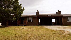 A two-story building with a garage entrance, a wooden deck, and a large tree to the left. - Paintbrush North- clean & quiet home with mountain views (West Yellowstone)