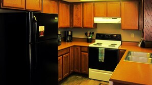 A kitchen with wooden cabinets, a black refrigerator, a white stove, and a stainless steel sink. - Paintbrush North- clean & quiet home with mountain views (West Yellowstone)