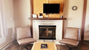 A living room with a fireplace, two armchairs, a coffee table, and a flat-screen TV mounted above the fireplace. - Paintbrush Grande - spacious & comfortable, perfect for families (West Yellowstone)