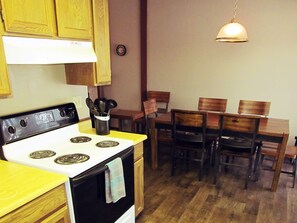 Une cuisine équipée d’une cuisinière, de meubles de rangement en bois, d’une table à manger avec des chaises et d’un luminaire suspendu.