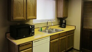 A compact kitchen with wooden cabinets, a microwave, a dishwasher, a sink, and a window with blinds. - Paintbrush Grande - spacious & comfortable, perfect for families (West Yellowstone)