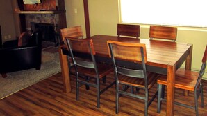 A dining room with a wooden table and chairs, a television on a stand, and a fireplace. - Sandhill East Home - Mountain Views, Portable A/C & 15 Minutes to Yellowstone (West Yellowstone)